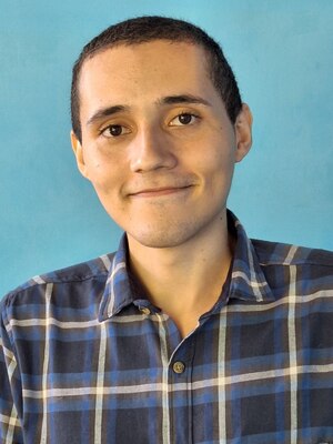 Un hombre joven con camisa a cuadros azul y blanca mirando a la cámara.